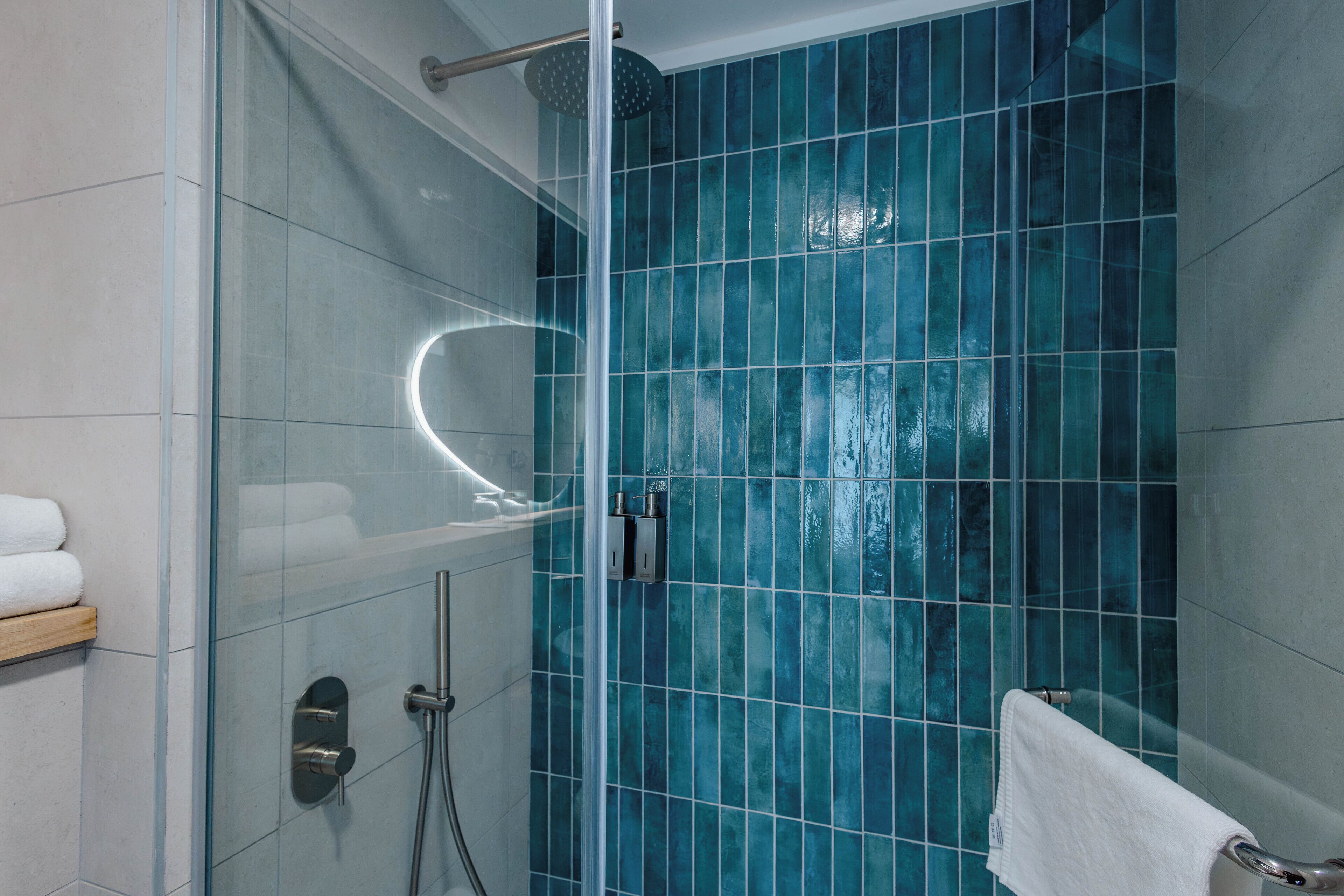 A modern bathroom with a glass-enclosed shower, a white towel on a rack, and a blue-tiled wall.