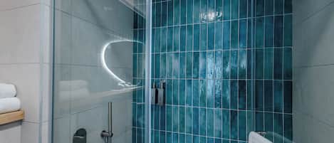 A modern bathroom with a glass-enclosed shower, a white towel on a rack, and a blue-tiled wall.