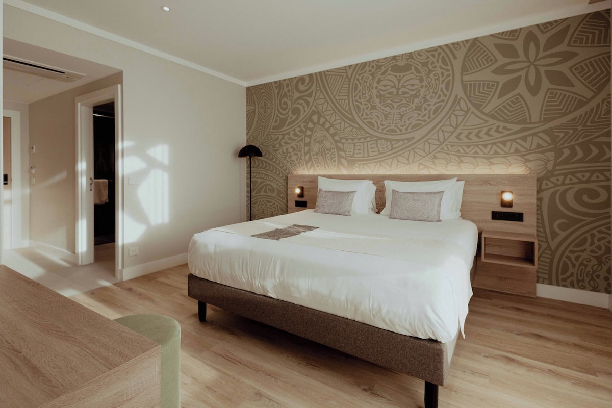 Une chambre moderne avec un grand lit, un plancher en bois, un papier peint à motifs et des lampes de chevet.