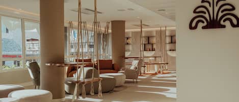 A modern hotel lobby with a large window, a hanging swing chair, and a decorative wall piece.