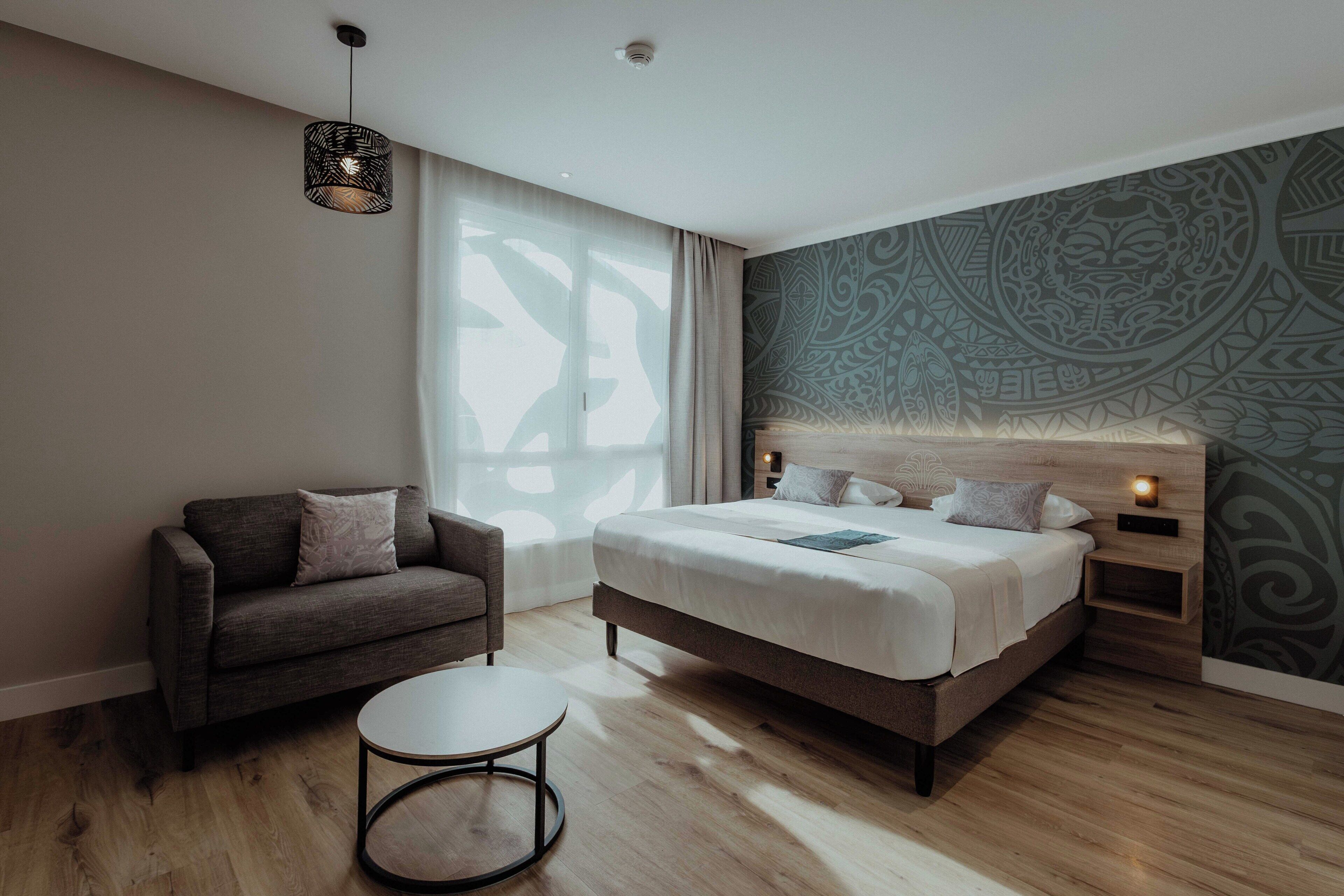 A modern bedroom with a bed, a sofa, a round table, and a patterned wall.
