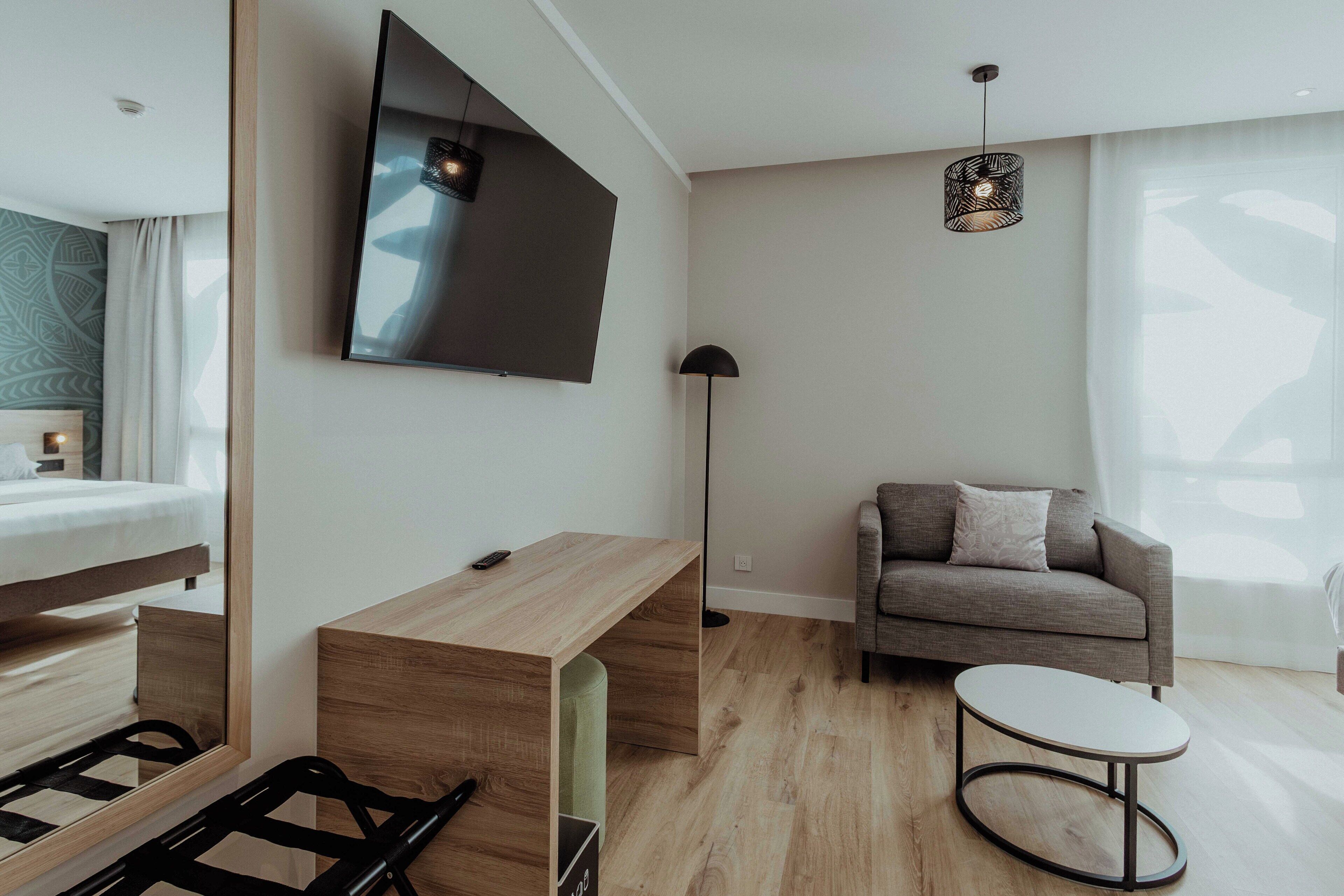 Ein modernes Wohnzimmer mit einem flachbildfernseher an der Wand, einer Couch, einem kleinen runden Tisch und einer Stehlampe.