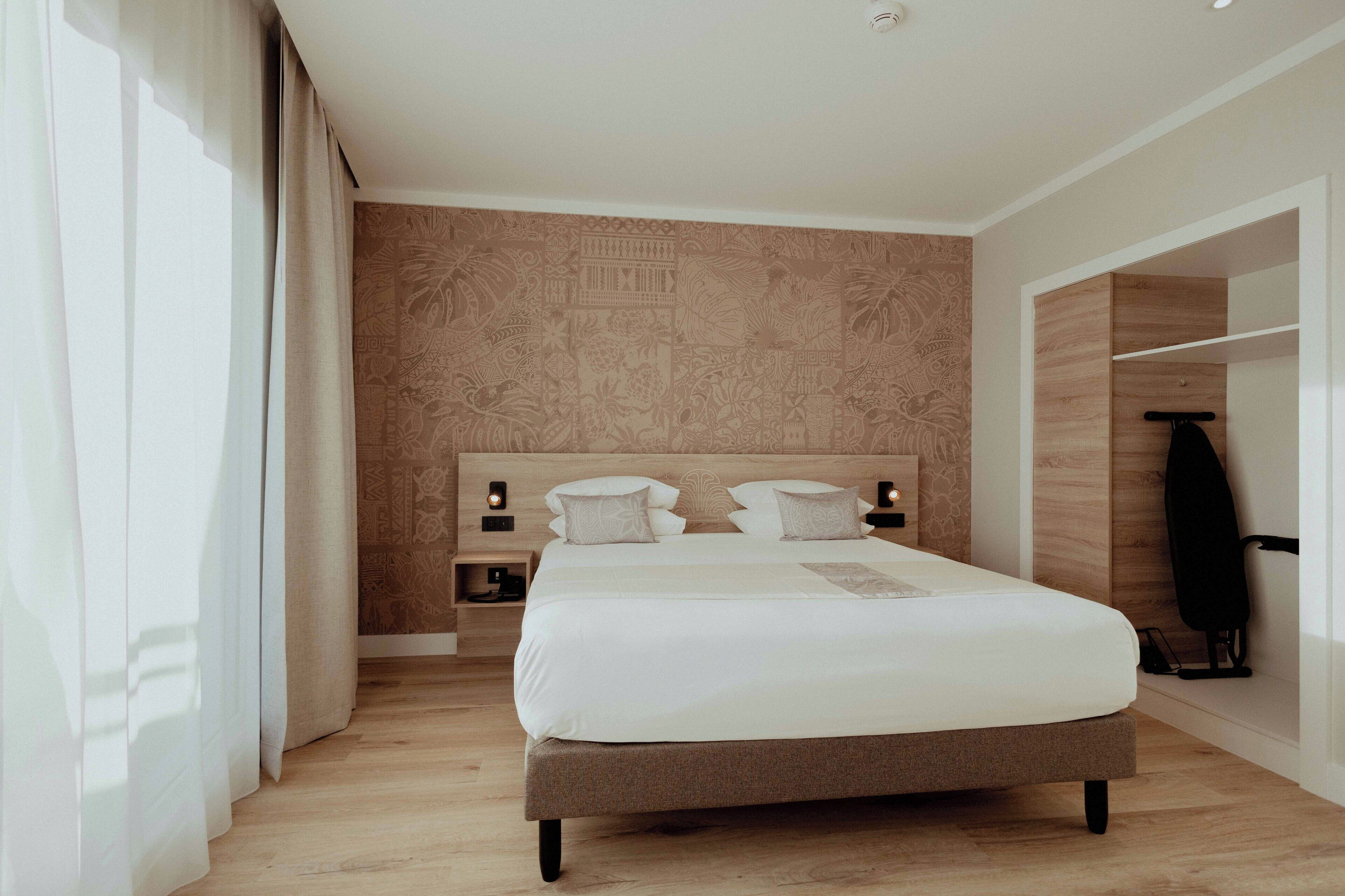 A modern hotel room with a large bed, wooden headboard, and a nightstand with a lamp.