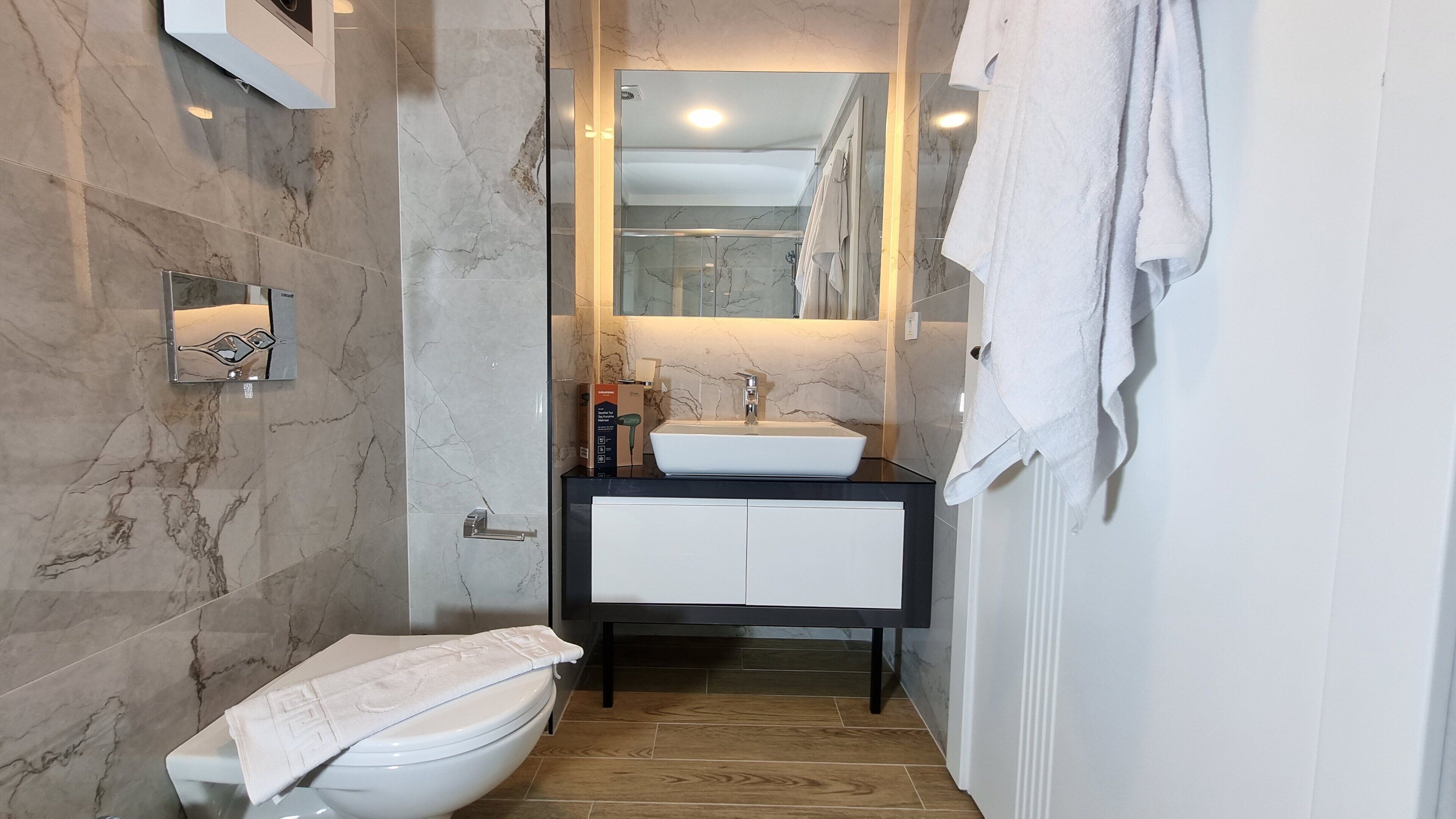 Ein Badezimmer mit einer weißen Toilette, einem Waschbecken mit Spiegel darüber und einem Handtuch an der Wand.