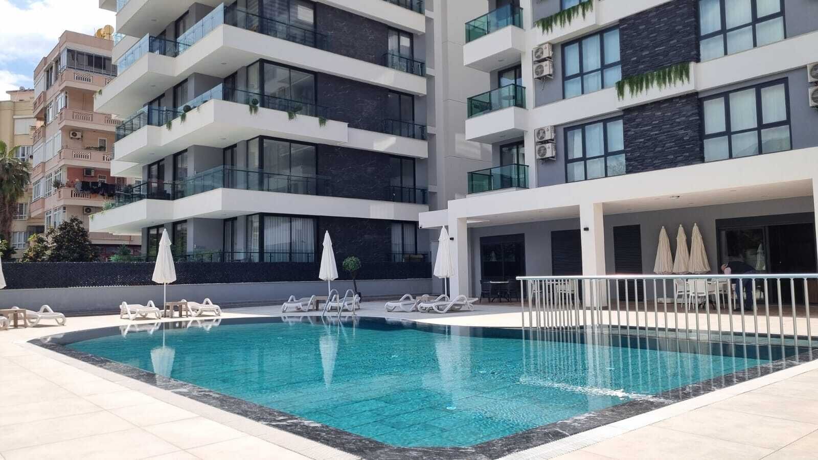 A modern hotel with a swimming pool, multiple balconies, and outdoor seating areas.