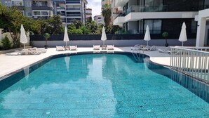 Ein Swimmingpool mit Liegestühlen und Sonnenschirmen, umgeben von einer niedrigen Mauer und einem Gebäude im Hintergrund.