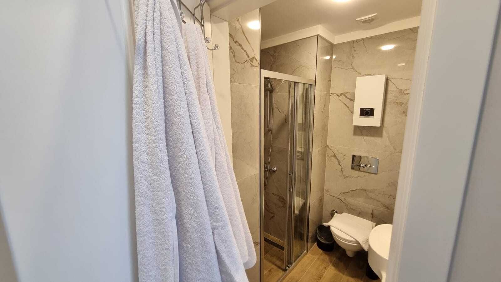 A modern bathroom with a glass-enclosed shower, a toilet, and a marble wall.