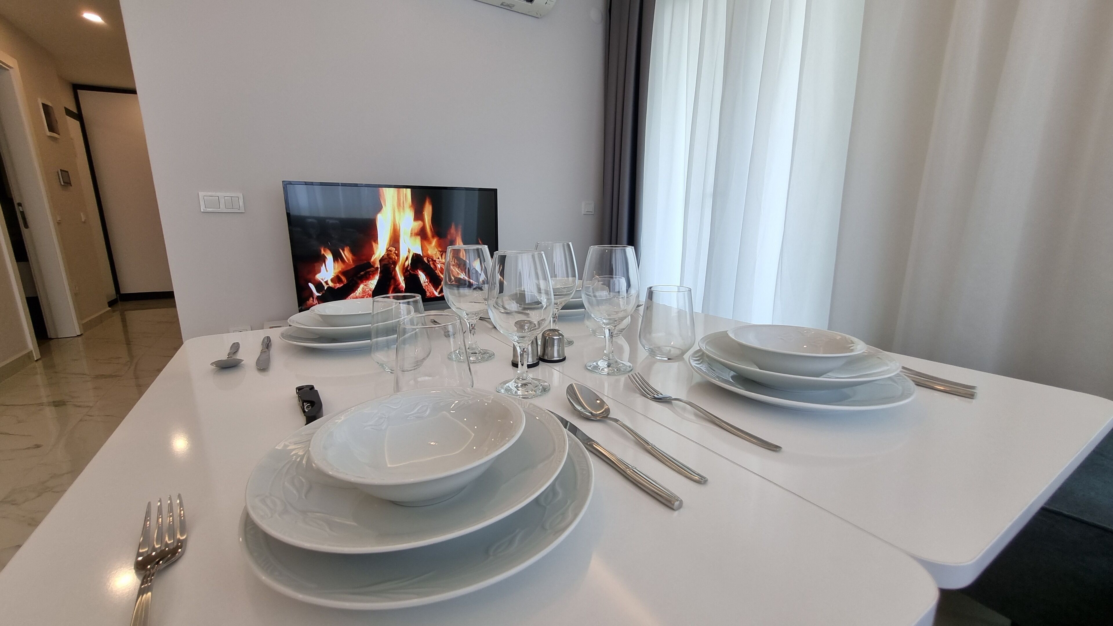 Een eettafel gedekt met borden, glazen, bestek en een televisie waarop een haard wordt getoond.