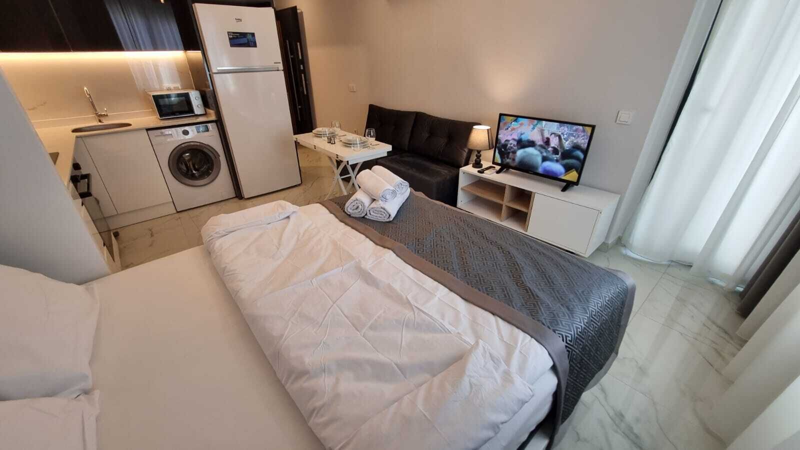 A hotel room with a bed, a small kitchenette, a TV, and a bathroom.