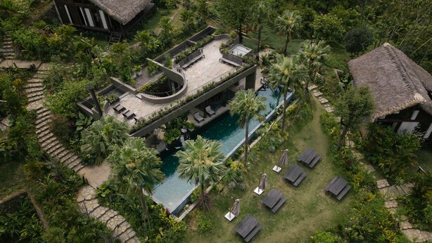 Un resort con piscina, sillones de descanso y un edificio con techo de paja.