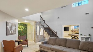Ein großzügiges Wohnzimmer mit einer Couch, Sesseln und einem Couchtisch. Eine Treppe führt auf eine höhere Ebene.