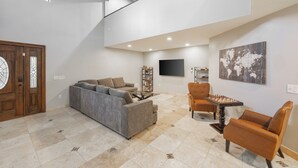 Ein geräumiges Wohnzimmer mit grauem Sofa, zwei Sesseln, einem Couchtisch und einem Schachtisch.