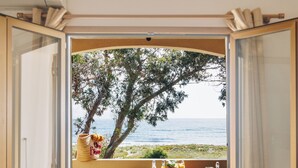 A room with an open window overlooking a beach, a table with breakfast items, and a hat on the floor. - Oro Biancu (Lucciana)