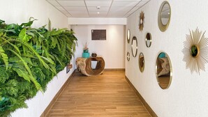 A hallway with a wooden floor, green plants on the left, and decorative mirrors on the right. - Oro Biancu (Lucciana)