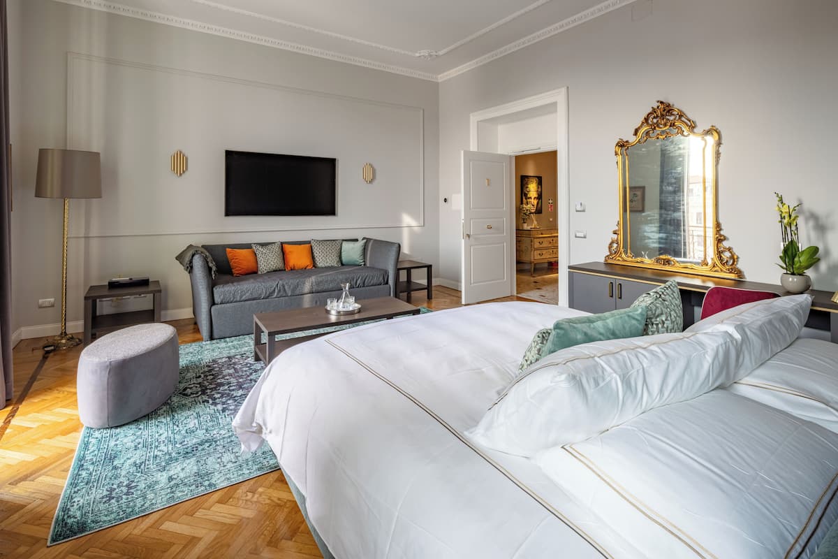 A modern bedroom with a large bed, a sofa, a TV, and a mirror.
