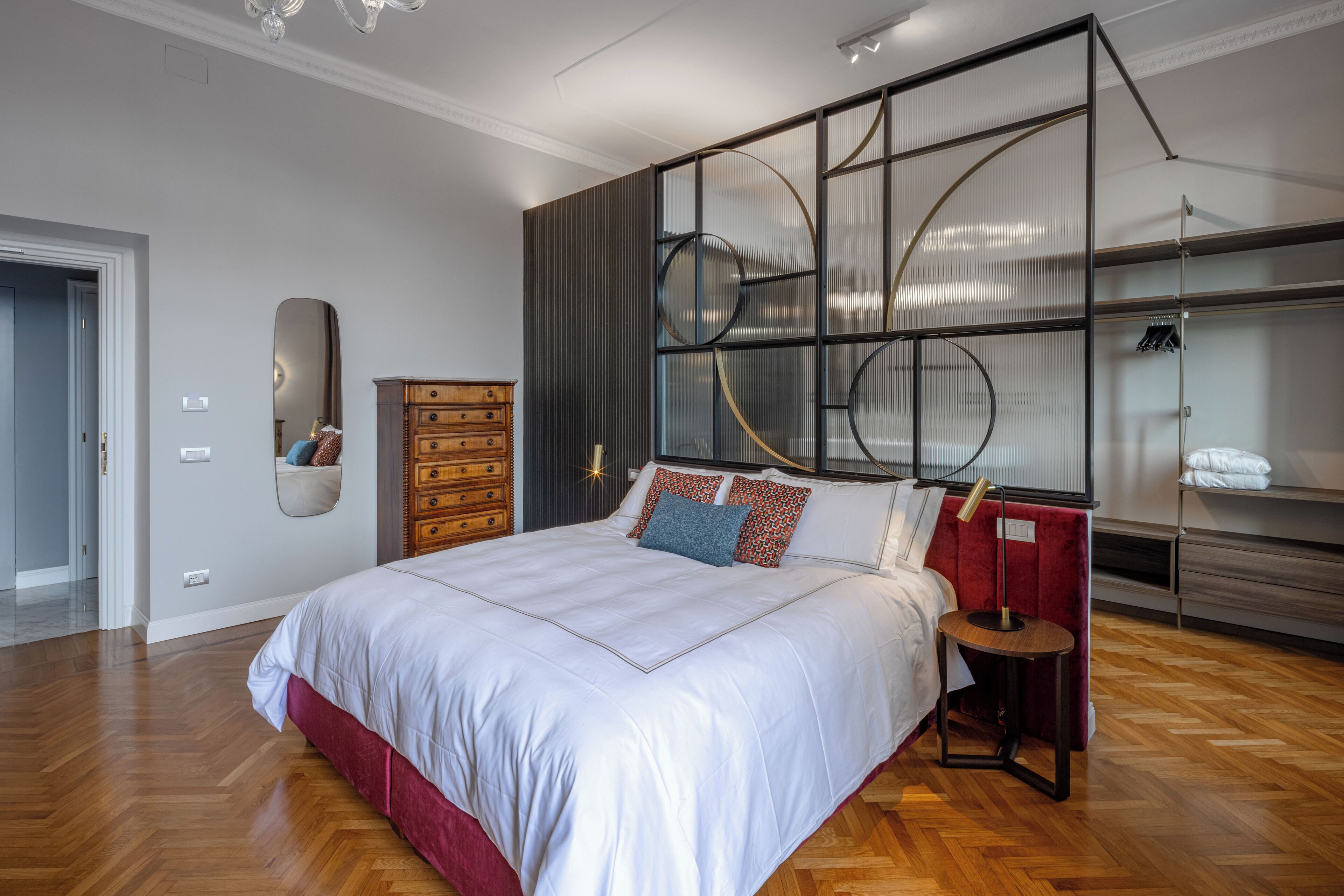 A modern bedroom with a large bed, a wooden dresser, a mirror, and a built-in shelving unit with circular designs.