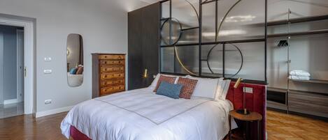 A modern bedroom with a large bed, a wooden dresser, a mirror, and a built-in shelving unit with circular designs.