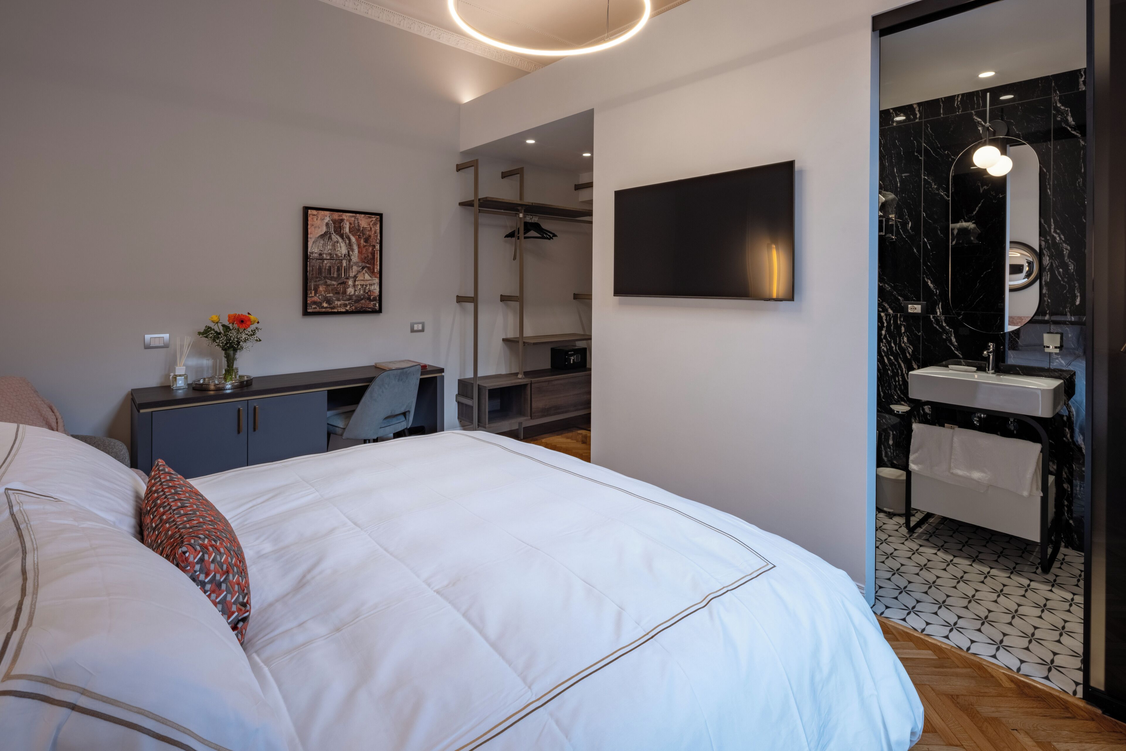 Habitació d'hotel moderna amb un llit gran, escriptori, armari i bany amb un lavabo de marbre i mirall.