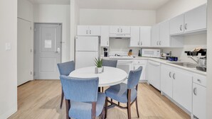 Une cuisine moderne avec des meubles blancs, un four à micro-ondes, un évier et une table à manger entourée de chaises bleues.