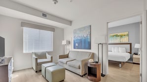 Una habitación de hotel moderna con sofá, una mesita, una mesita de noche, un televisor y un cuadro en la pared.