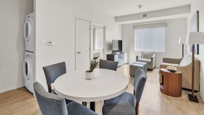 Una sala de estar moderna con una mesa redonda blanca, sillas grises, un televisor, un sofá y una lámpara.