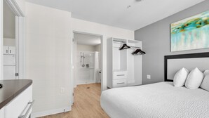 A modern bedroom with a large bed, a walk-in closet, and a shower area.
