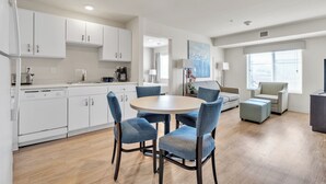 A modern kitchen with white cabinets, a round dining table with blue chairs, and a seating area with a sofa and ottoman. - Simplicity At the Rim 1216 I Comfy 2 Bed 2 Bath (San Antonio)