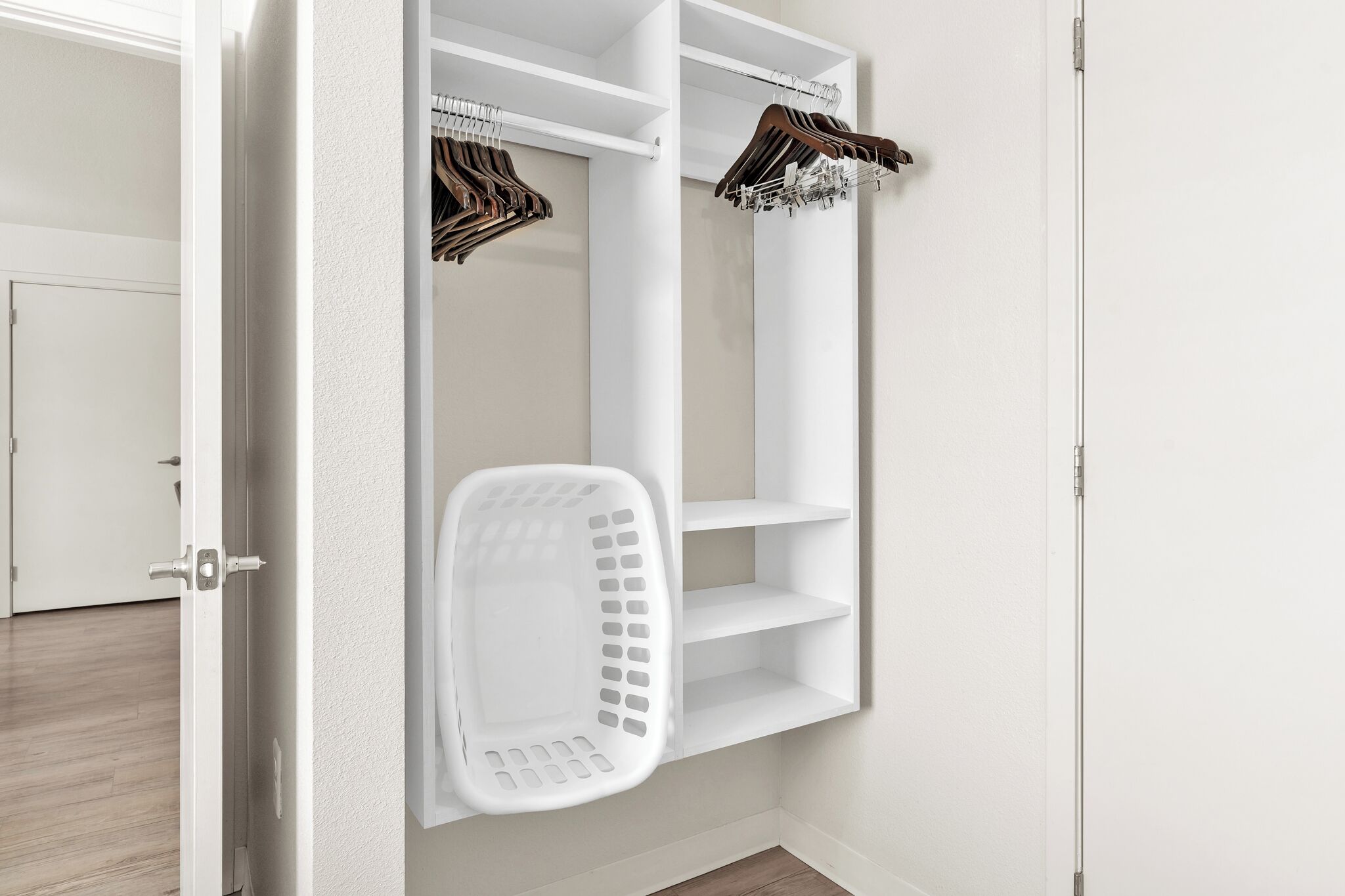 A white closet with shelves and a hanging rack, a white laundry basket, and a door.