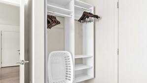 A white closet with shelves and a hanging rack, a white laundry basket, and a door.