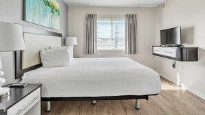A modern hotel room with a large bed, a flat-screen TV, a desk with a lamp, and a painting on the wall.