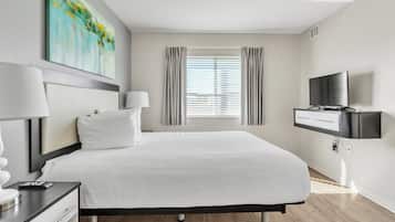 Una habitación de hotel moderna con una cama grande, un televisor de pantalla plana, un escritorio con una lámpara y un cuadro en la pared.