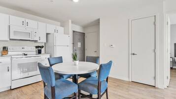Una cocina moderna con electrodomésticos blancos, una mesa de comedor con sillas azules y una puerta que da a otra habitación.