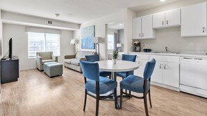 A modern living room with a round dining table, blue upholstered chairs, a grey sofa, and a flat-screen TV.