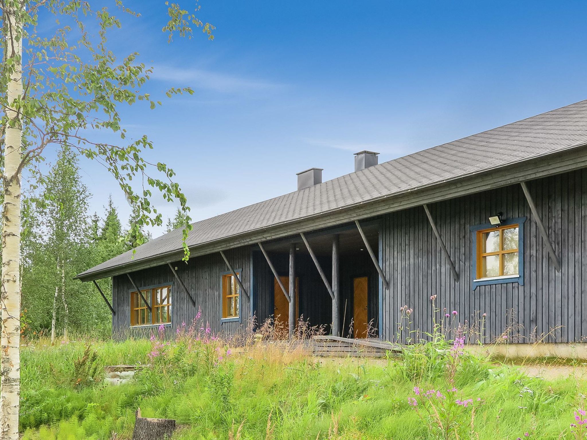 A rustic wooden cabin with a porch, surrounded by lush greenery and wildflowers.
