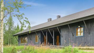 A rustic wooden cabin with a porch, surrounded by lush greenery and wildflowers.