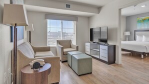 A modern hotel room with a sofa, ottoman, TV, and a bed.