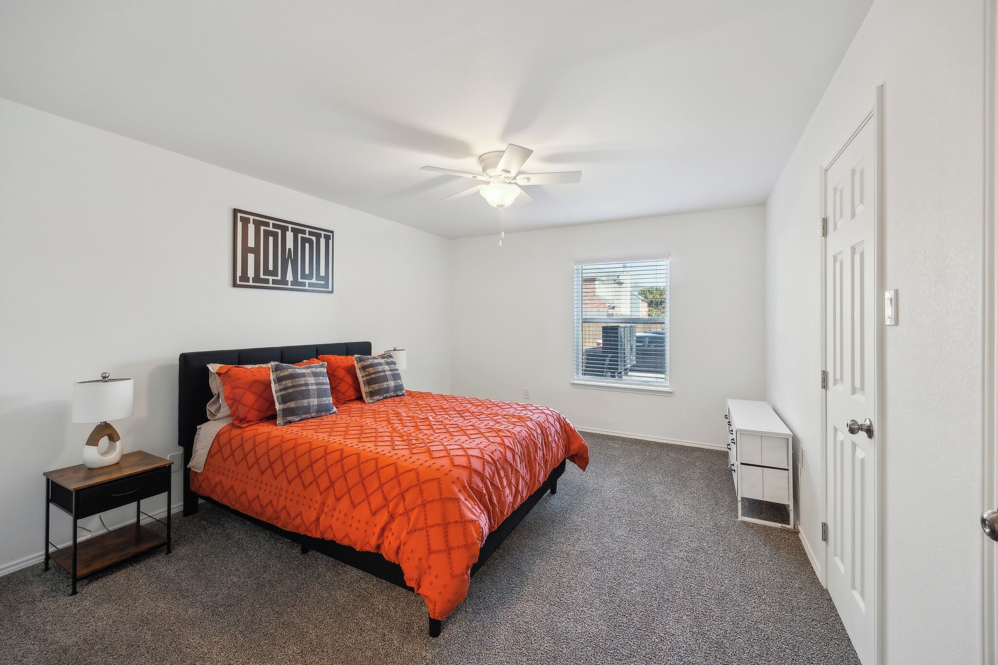 Une chambre à coucher comprenant un lit, une table de chevet, un ventilateur de plafond, une fenêtre et une porte.