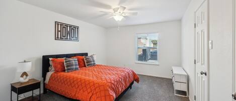 Une chambre à coucher comprenant un lit, une table de chevet, un ventilateur de plafond, une fenêtre et une porte.