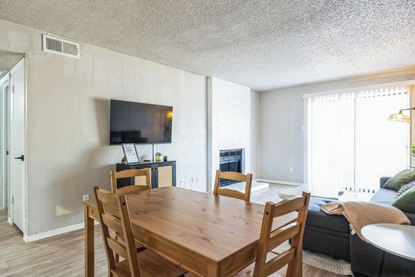 A dining area with a wooden table and chairs, a flat-screen TV mounted on the wall, and a fireplace in the background.