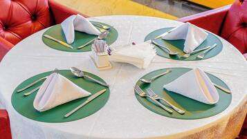 Mesa redonda para comer con individuales verdes y servilletas blancas dobladas en forma de conos, cubiertos y un pequeño jarrón blanco con flores.