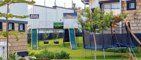 A residential backyard with a trampoline, a slide, and a swing set.