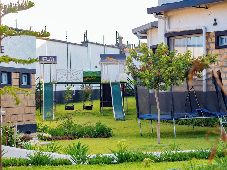 A residential backyard with a trampoline, a slide, and a swing set.