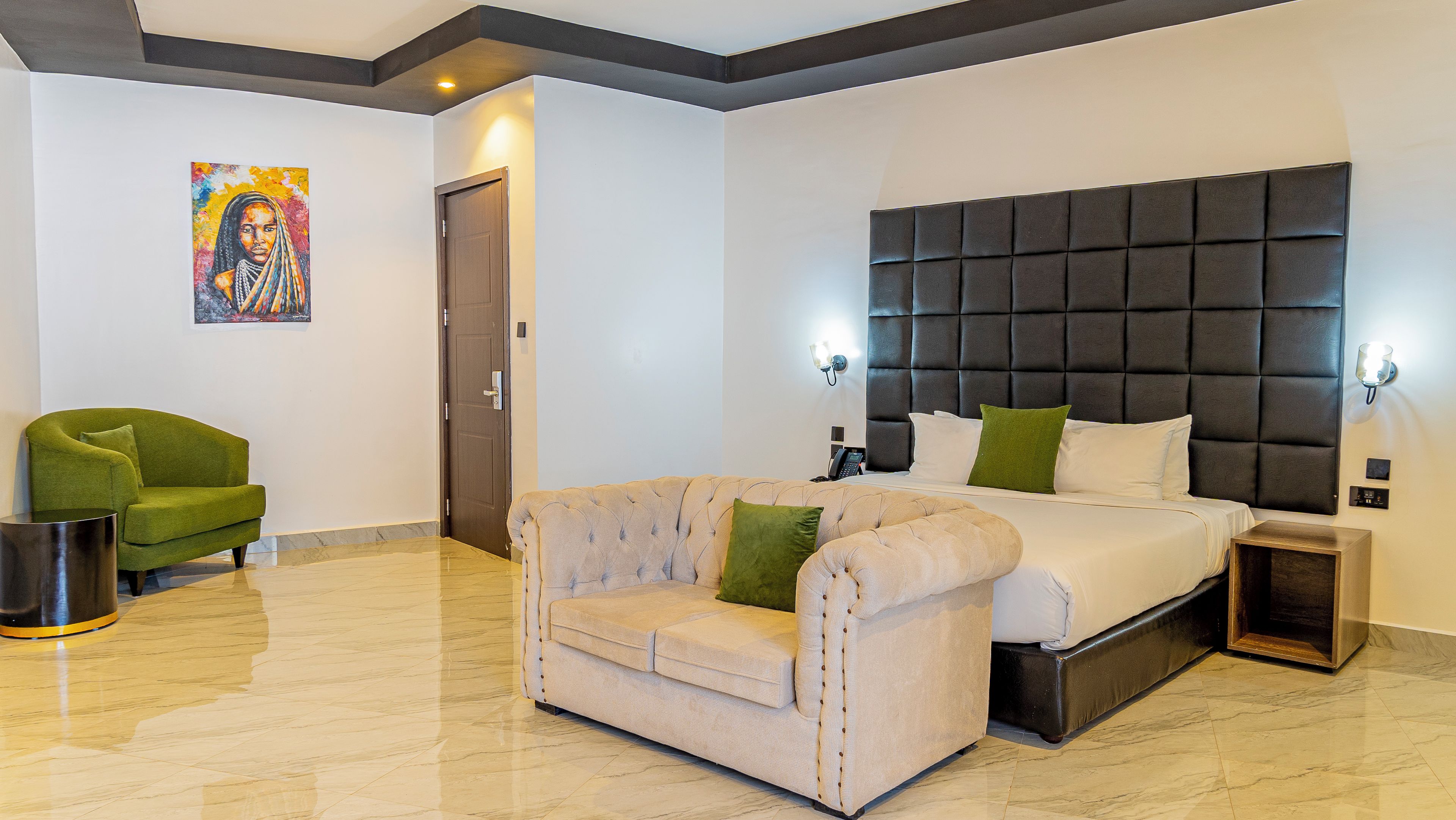 A hotel room with a bed, a sofa, a green armchair, a marble floor, and a painting on the wall.