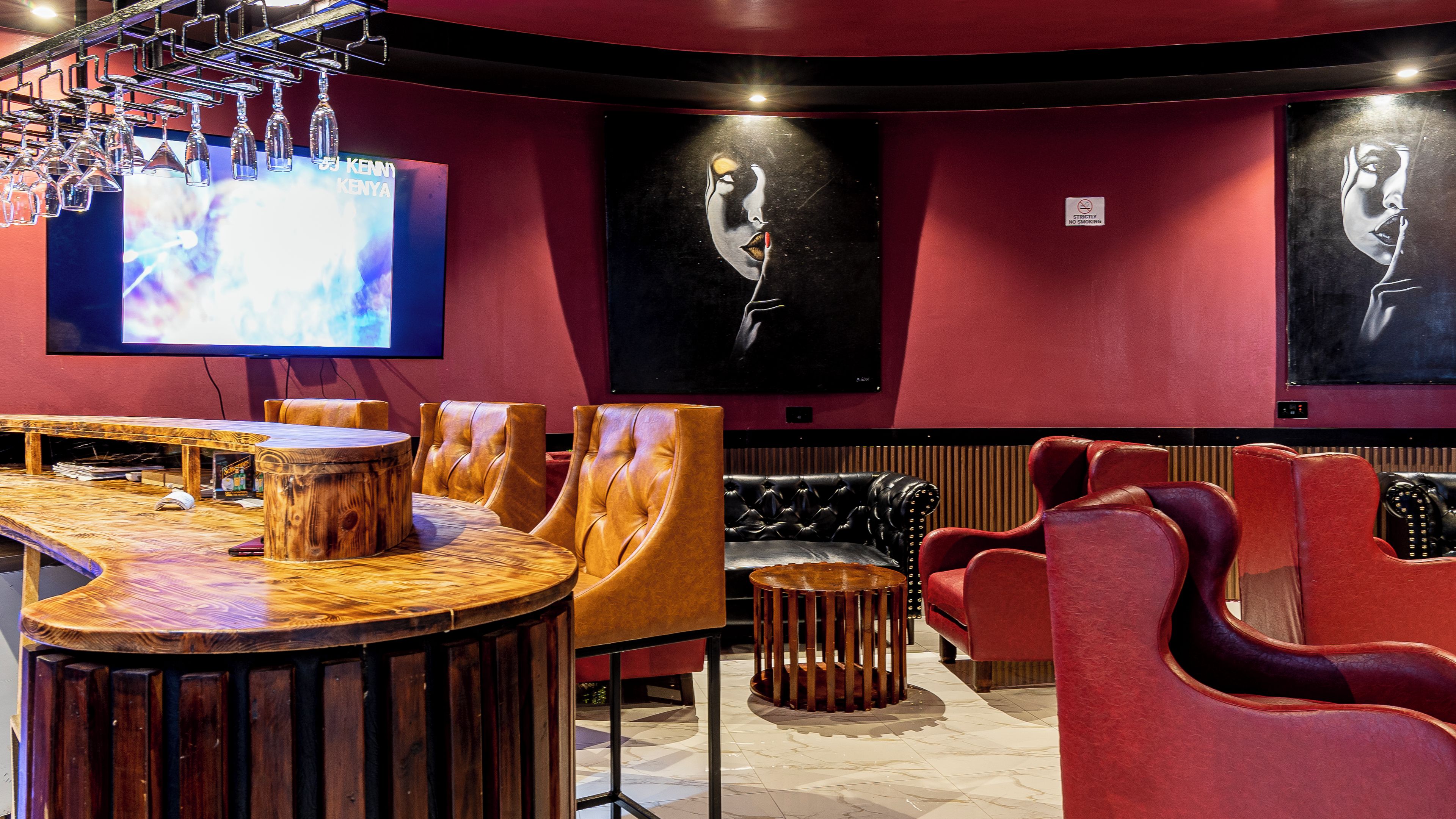 A bar area with a wooden bar counter, leather seating, and a television screen displaying a show.