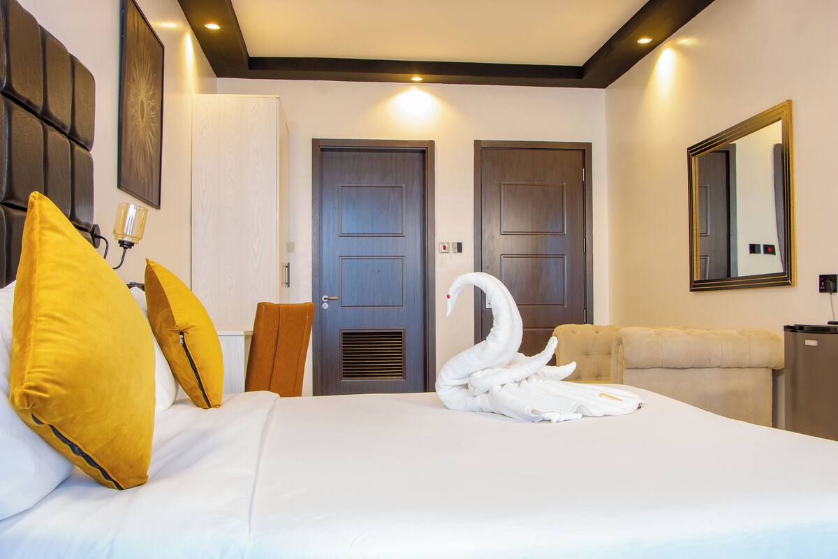 Quarto de hotel com cama, duas portas, espelho e cisne de toalha.