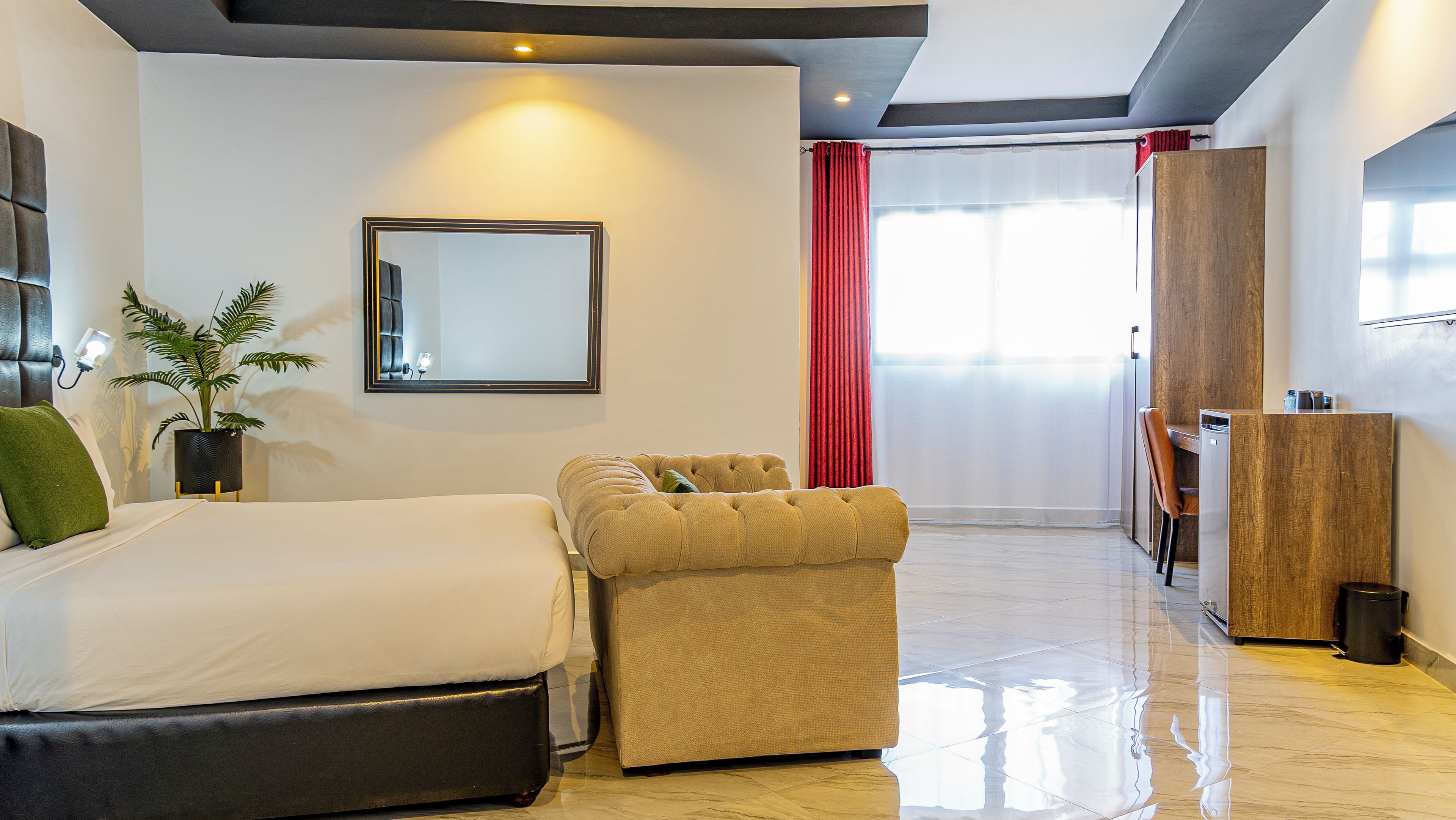 Habitación de hotel moderna con cama, zona de estar, espejo, planta y vista al exterior.