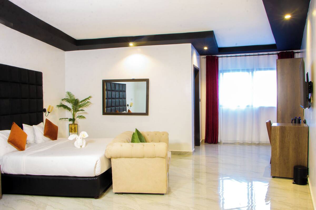 Quarto de hotel com cama, sofá, espelho, planta e um armário de madeira.