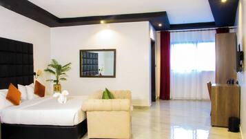 A hotel room with a bed, a sofa, a mirror, a plant, and a wooden cabinet.