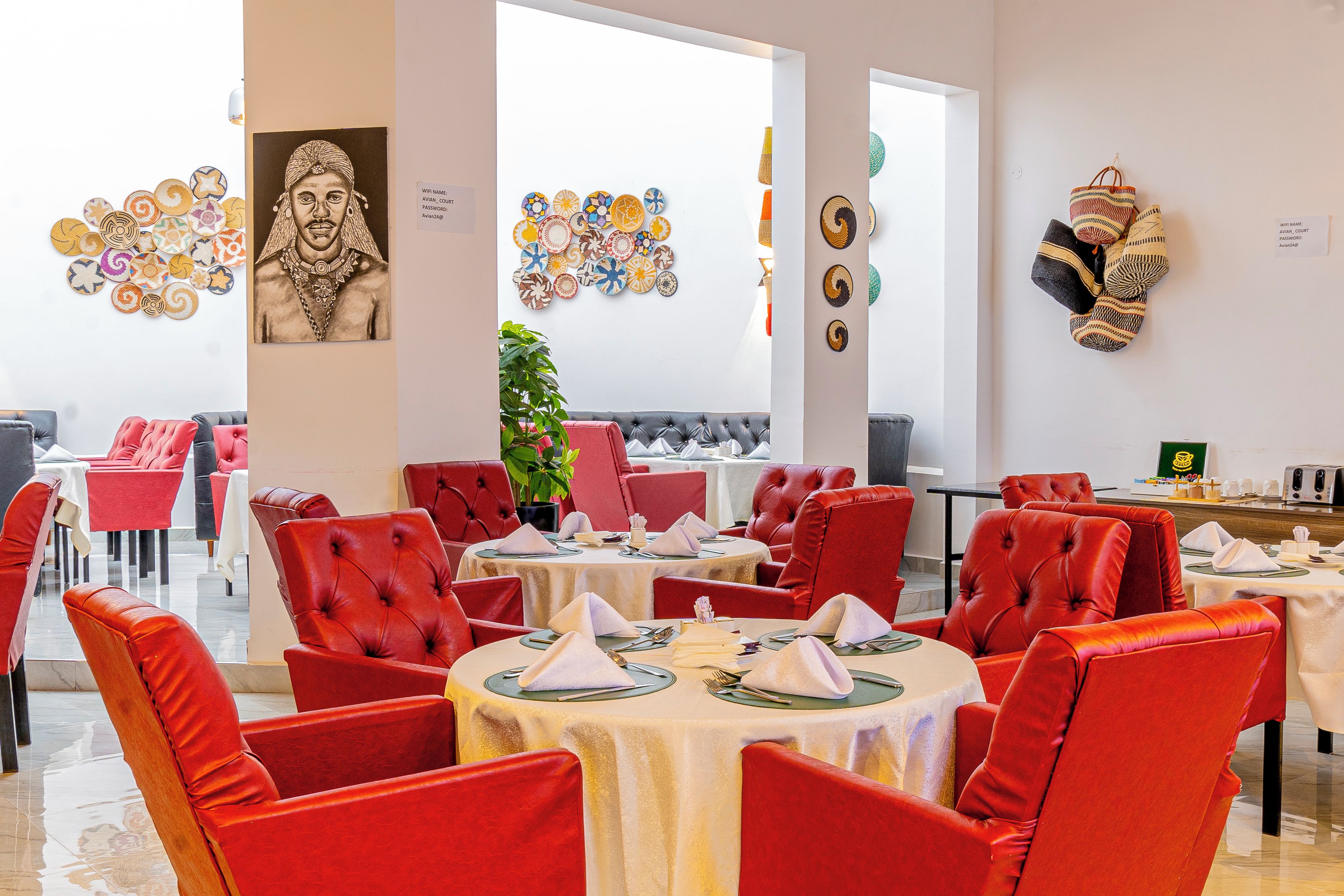 A restaurant with red upholstered chairs, round tables, and various wall decorations including woven baskets and a framed portrait.