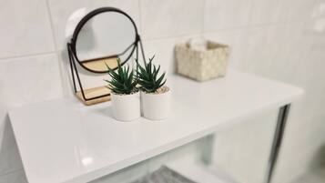 A white shelf with two potted plants, a small decorative box, and a mirror.